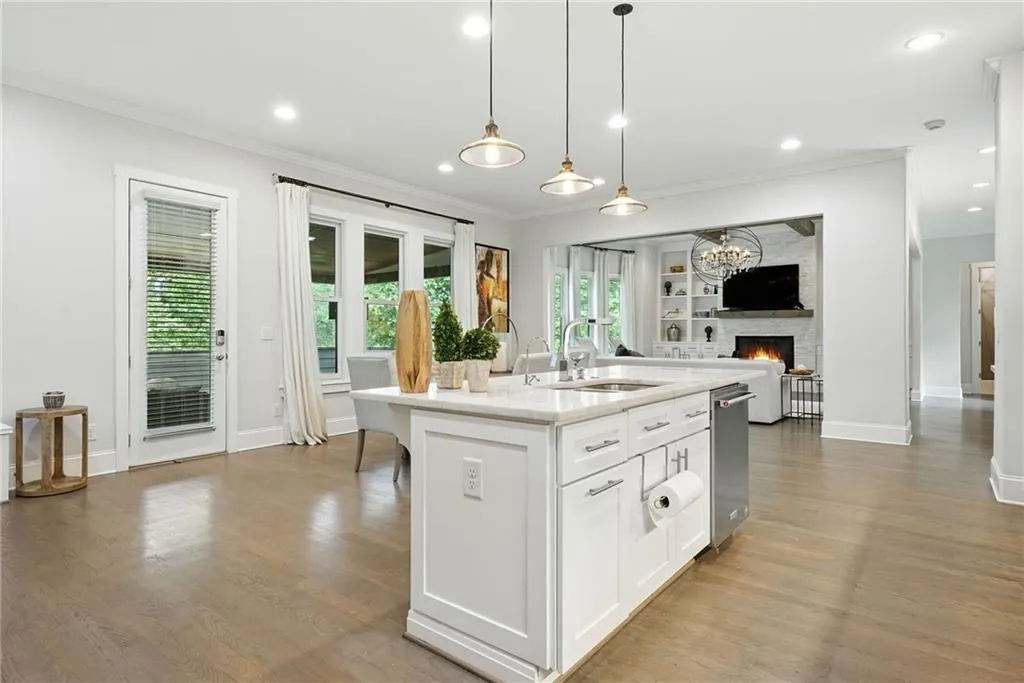 Kitchen with white cabinets, light stone counters, a large fireplace, an island with sink, and light wood finished floors