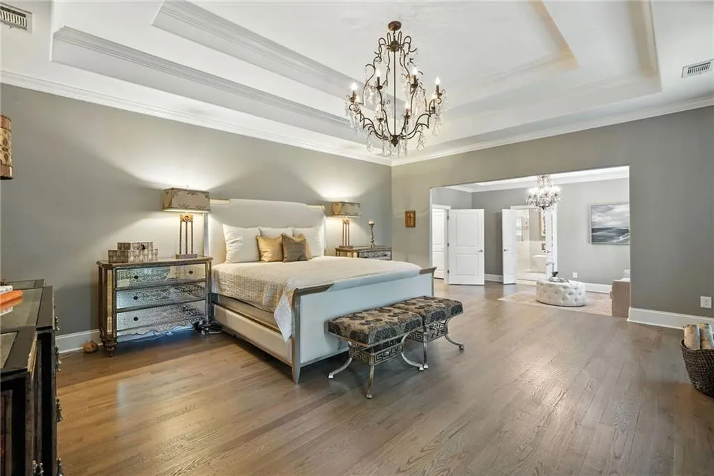 Bedroom with a tray ceiling, a chandelier, wood finished floors, ornamental molding, and ensuite bathroom