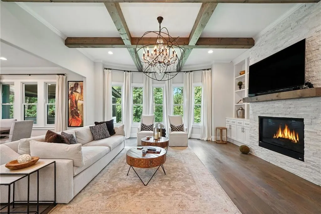 Living area featuring wood finished floors, beam ceiling, ornamental molding, a stone fireplace, and recessed lighting
