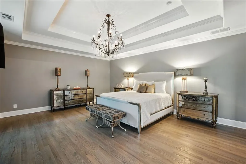 Bedroom with a raised ceiling, a chandelier, wood finished floors, and crown molding