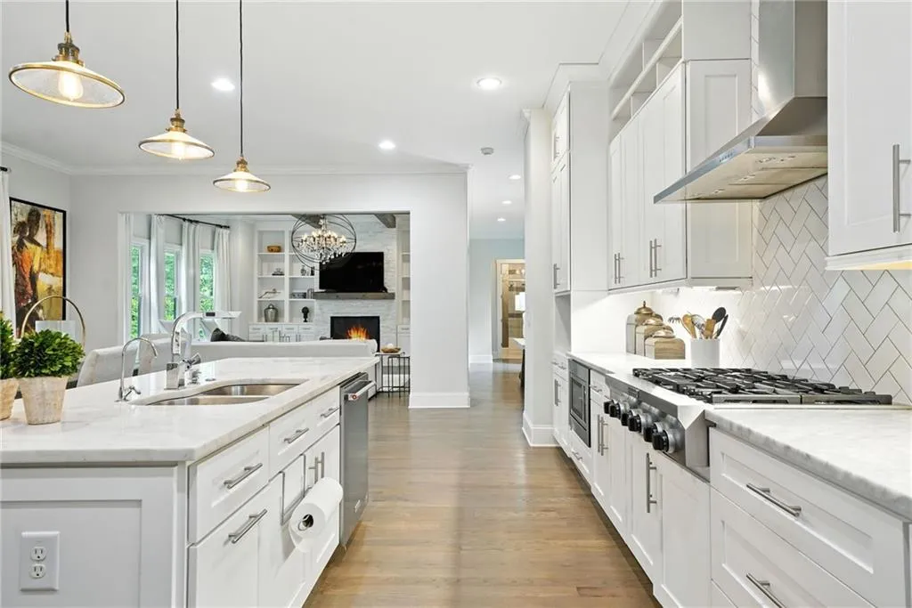 Kitchen with white cabinets, wall chimney exhaust hood, pendant lighting, stainless steel appliances, and light stone countertops