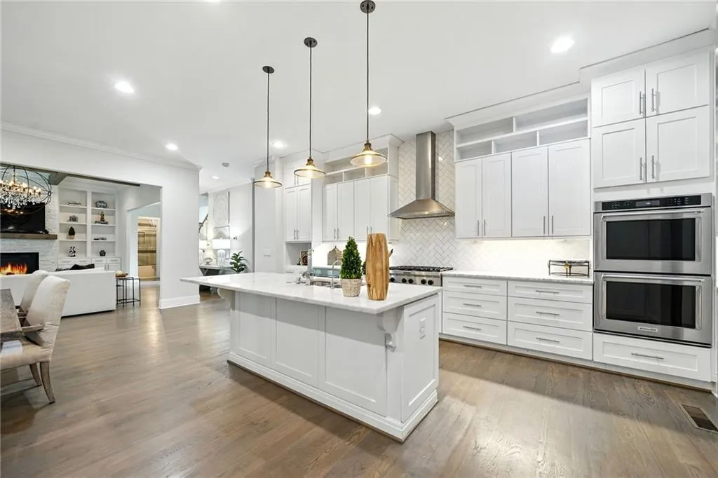 Kitchen with white cabinets, backsplash, stainless steel double oven, hanging light fixtures, and open floor plan
