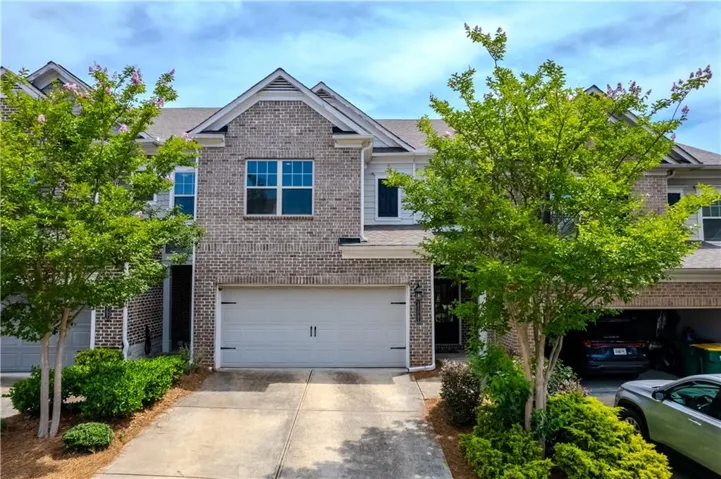 Brick exterior with white garage door, gabled roofline, and established landscaping
