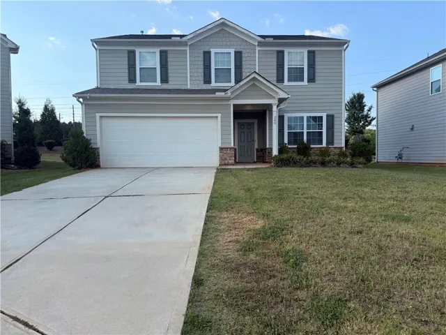 Two-story residence featuring light gray siding, dark green shutters, an attached garage, and a concrete driveway