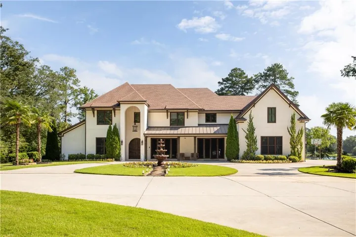 Stucco exterior with a tiled roof, featuring a circular driveway, a multi-tiered fountain, and established landscaping