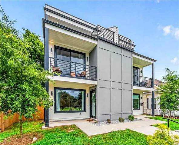 Modern exterior with a flat roofline, a balcony and rooftop deck featuring black metal railings, large windows, and a concrete walkway