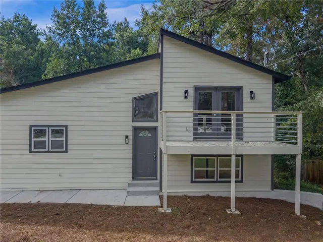 Contemporary exterior with light siding and dark trim, featuring a prominent front balcony with metal railings and French doors
