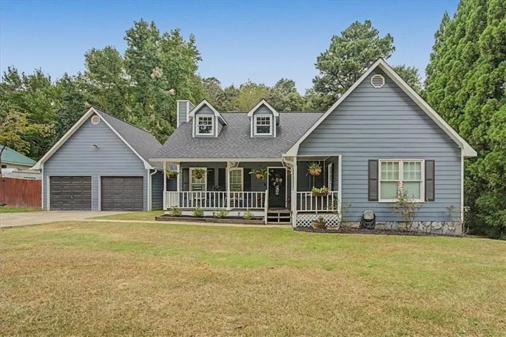 Front exterior with blue siding, a covered porch, white railings, a two-car garage, and dormer windows