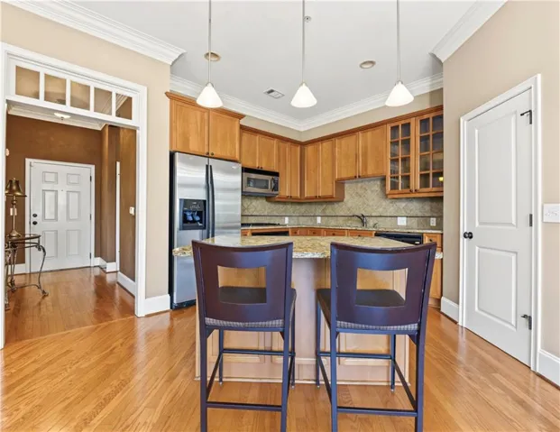Kitchen featuring wood cabinetry, stainless steel appliances, a stone countertop island, tile backsplash, and wood-finish flooring