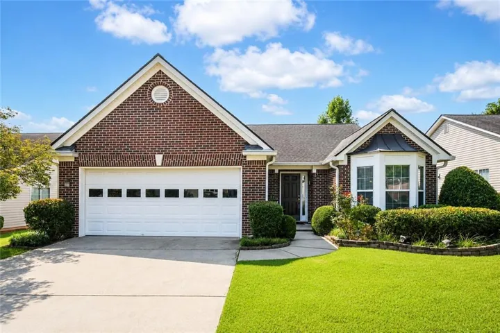 Brick facade home featuring a two-car garage, bay window, landscaped front yard, and concrete driveway