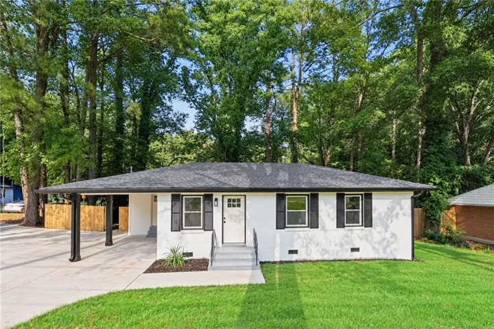 White exterior with black shutters, dark shingle roof, paved driveway, and covered carport