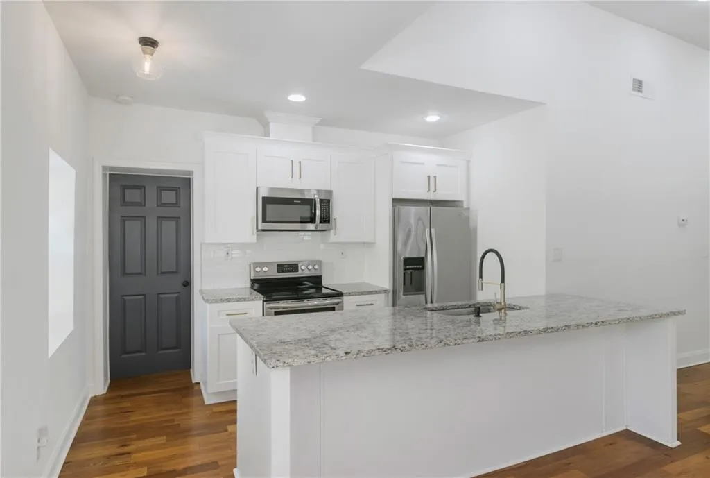 Kitchen featuring decorative backsplash, appliances with stainless steel finishes, white cabinetry, recessed lighting, and light stone counters