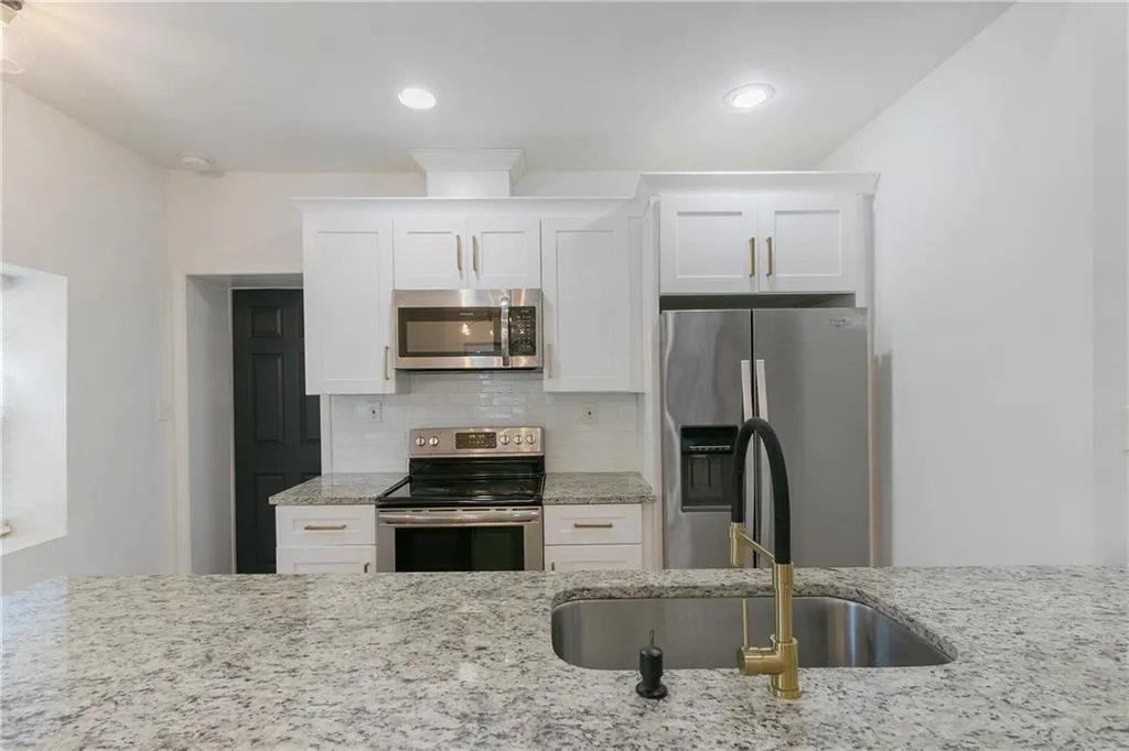 Kitchen with stainless steel appliances, backsplash, white cabinetry, light stone countertops, and recessed lighting