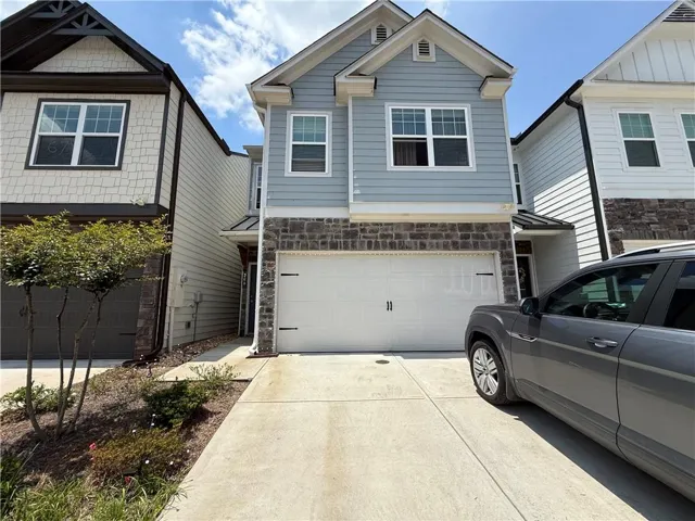 Multi-story residence featuring light blue horizontal siding, a stone facade, and a two-car garage with a white door