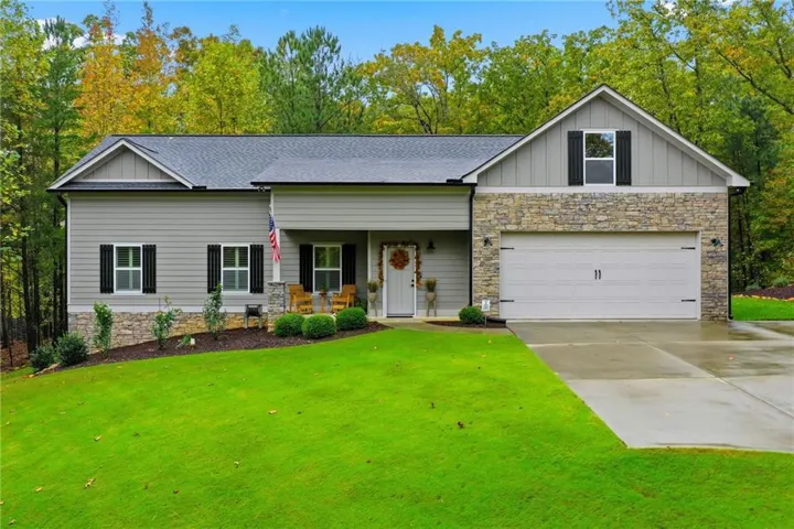 Contemporary ranch-style residence featuring a gray siding and stone facade, a two-car garage, a covered front porch, and a lush green lawn