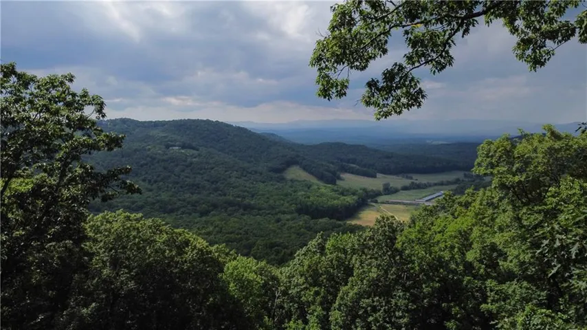 Looking north, you will see rolling mountain landscape with dense tree cover, visible distant valley, and expansive sky