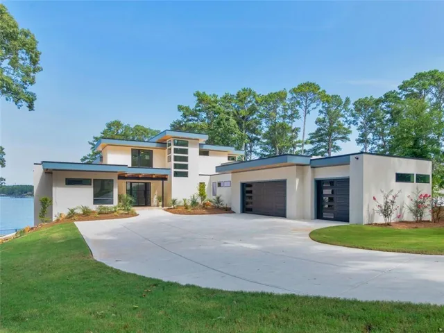 Modern stucco exterior featuring a flat roofline, expansive driveway, attached two-car garage with contemporary doors, and multiple large windows