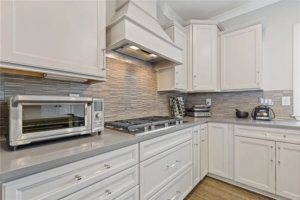 Kitchen with white cabinetry, decorative backsplash, stainless steel gas cooktop, and dark wood-style flooring