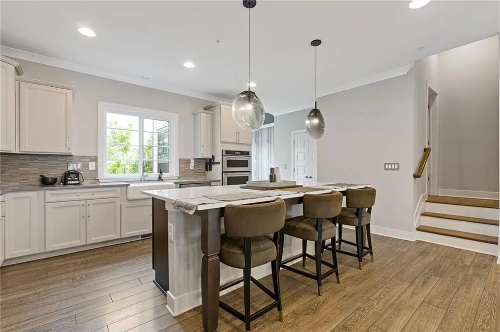 Two tone kitchen with dark wood-type flooring, a breakfast bar, crown molding, a kitchen island, and decorative backsplash