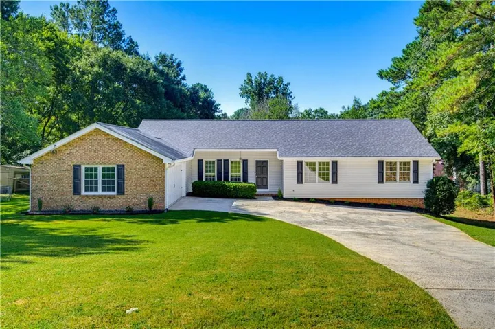 Brick and siding exterior with a dark-tone roof, featuring a curved concrete driveway and mature landscaping