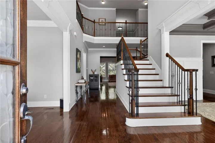 Grand foyer featuring rich wood-finish flooring, a multi-story staircase with wrought iron balusters and wood handrails, recessed lighting, and crisp white trimwork