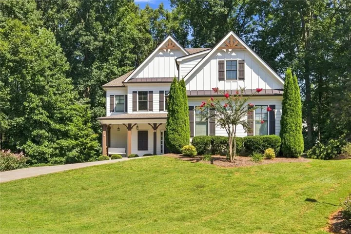 White board and batten exterior with dark shutters, prominent gables, and a front porch with wood columns