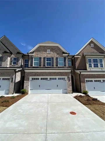 Brick exterior featuring a two-car garage, concrete driveway, and contrasting dark shutters