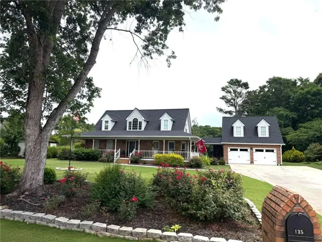 Brick facade residence with a covered front porch featuring white railings, dormer windows, and an attached two-car garage with white doors