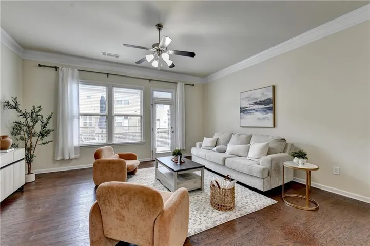 Wood-finish flooring, crown molding, a ceiling fan with integrated lighting, and multiple windows with blinds