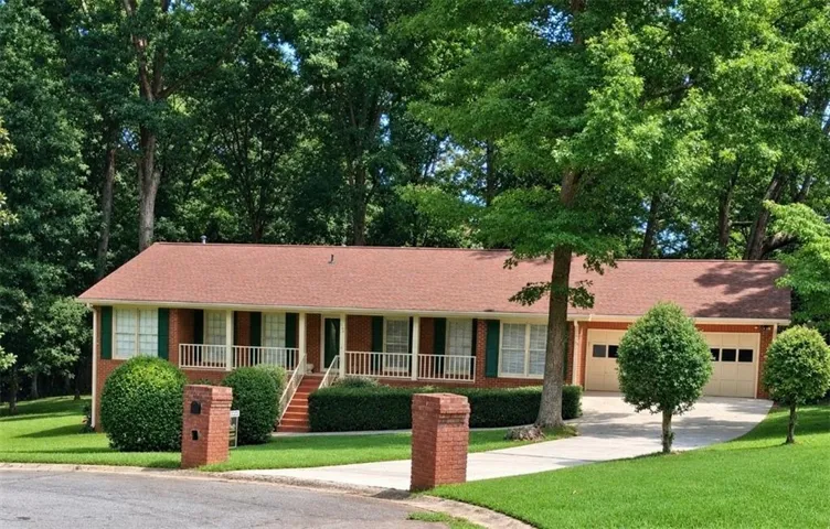 Brick exterior with green window shutters, a front porch featuring white railings, and an attached two-car garage
