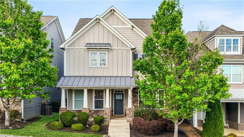 Contemporary architectural style featuring a multi-story facade with board and batten siding, stone accents, a covered front porch with columns, a dark panel front door, and a metal awning over the lower-level porch
