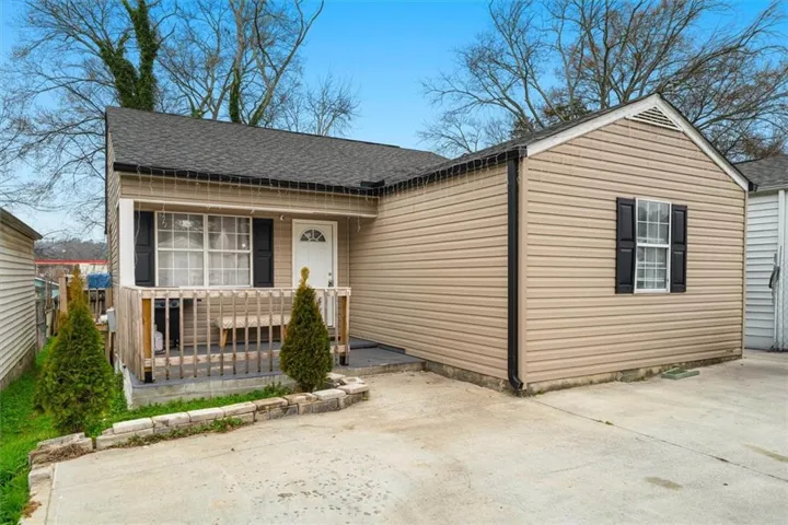 Exterior featuring tan horizontal siding, a wooden front porch, a dark gray shingle roof, and a concrete driveway