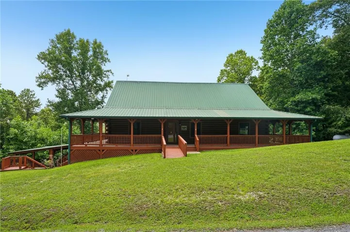 Log cabin exterior with a green metal roof, a full-length covered porch, and a wooden ramp entry