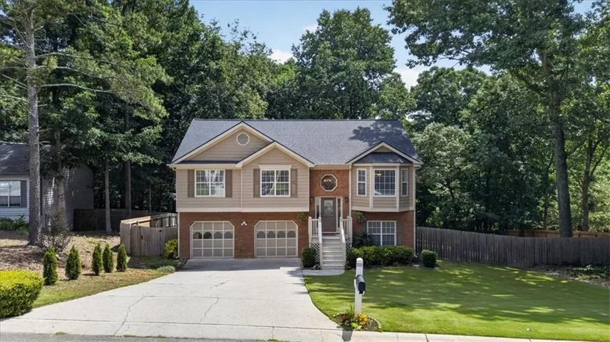 Two-story residence featuring a brick and siding exterior, an attached two-car garage with arched paneling, a concrete driveway, a front lawn, and mature perimeter trees