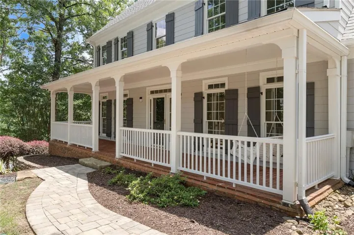 Expansive covered front porch featuring white railing, columns, and a brick foundation
