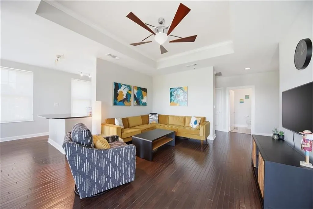 Living area featuring crown molding, dark wood-style flooring, ceiling fan, and a raised ceiling