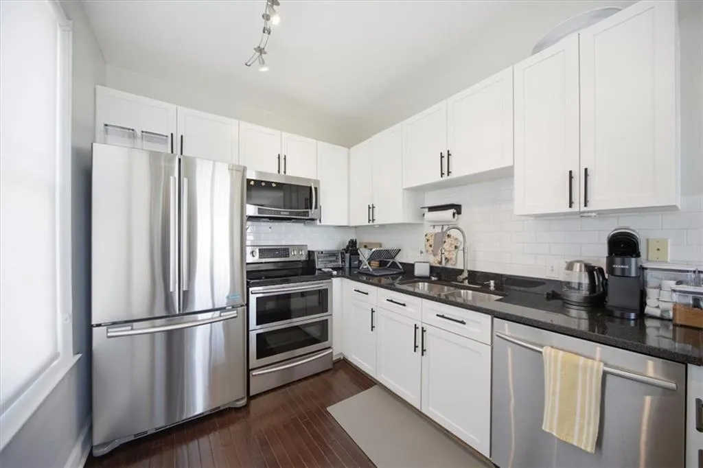 Kitchen with stainless steel appliances, white cabinets, dark stone counters, decorative backsplash, and dark wood-type flooring