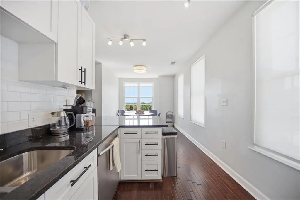 Kitchen featuring a peninsula, dark stone counters, white cabinets, dark wood-type flooring, and stainless steel dishwasher