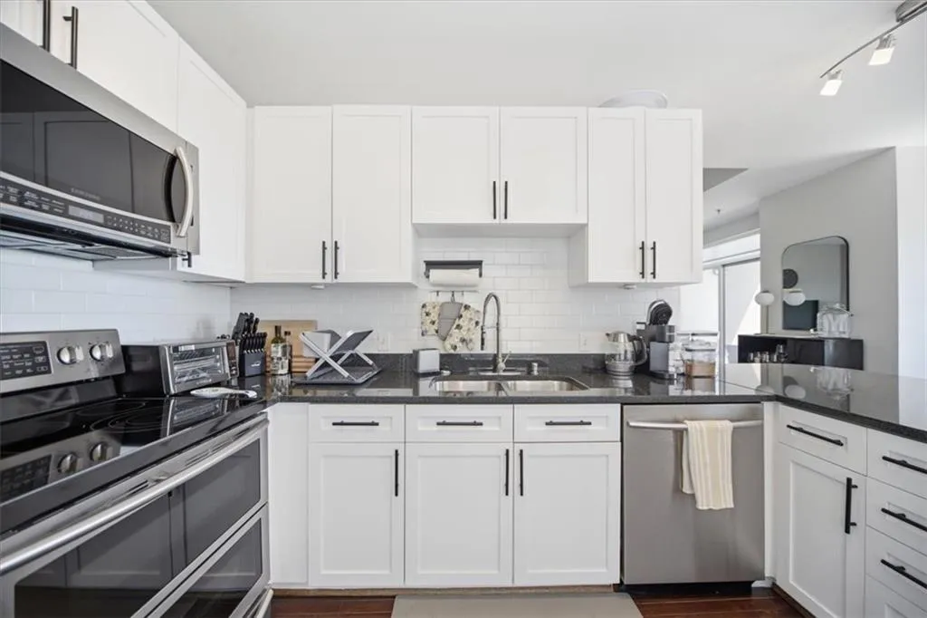 Kitchen featuring stainless steel appliances, white cabinetry, and dark stone countertops