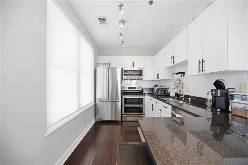 Kitchen with white cabinetry, dark stone countertops, stainless steel appliances, dark wood-type flooring, and tasteful backsplash