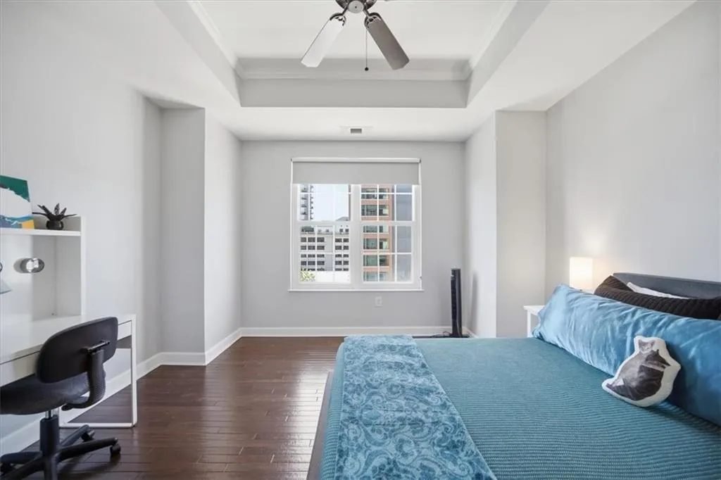Bedroom featuring crown molding, dark wood-type flooring, a ceiling fan, a raised ceiling, and a desk