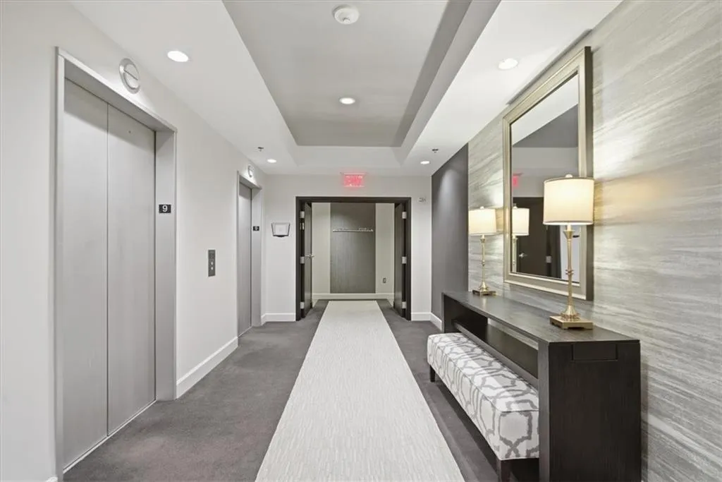Hall with elevator, dark colored carpet, a tray ceiling, and recessed lighting