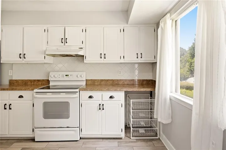 Kitchen featuring white cabinetry with dark hardware, a white electric range with overhead ventilation, a diamond-patterned tile backsplash, and wood-finish flooring