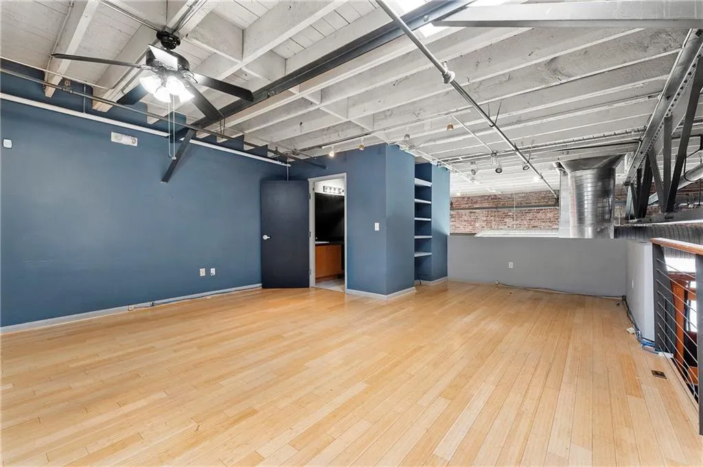 Basement with light wood finished floors, ceiling fan, and brick wall