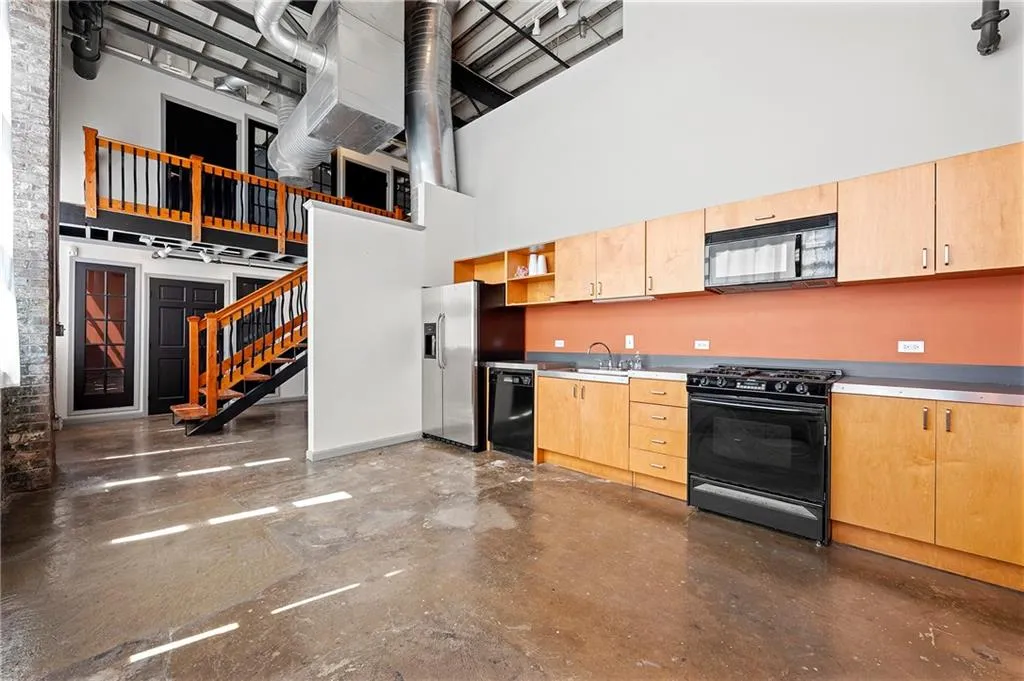 Kitchen featuring black appliances, light brown cabinets, a towering ceiling, concrete flooring, and light countertops