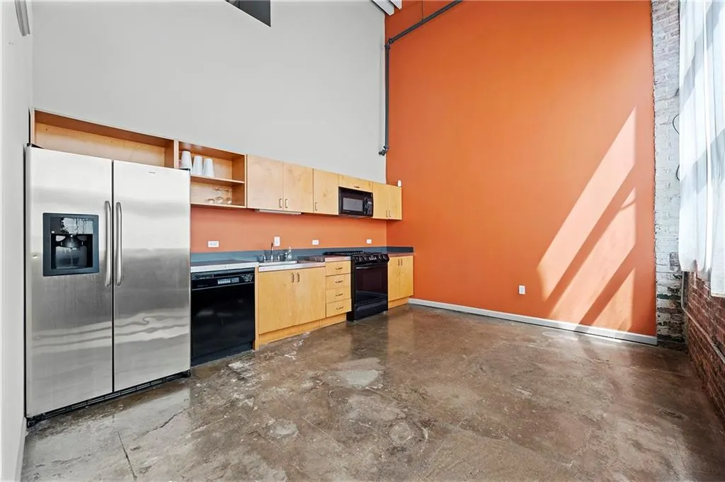 Kitchen with black appliances, a high ceiling, light brown cabinetry, open shelves, and concrete flooring