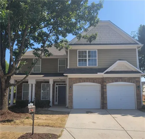 Two-story residence featuring a stone and siding exterior, a two-car garage, multiple windows, and a covered entry