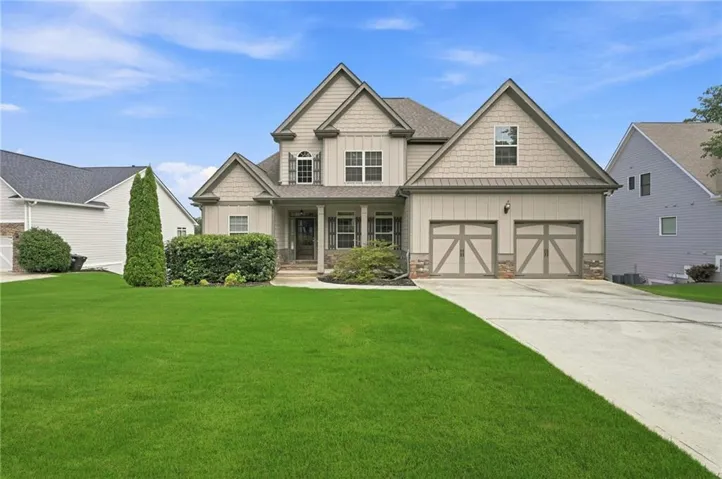 Traditional-style home featuring a two-car garage with carriage-style doors, stone accents, and a covered front porch