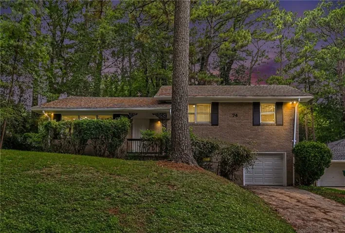 Brick exterior with dark shutters, attached garage with a panel door, and a front entry with a small porch and railing