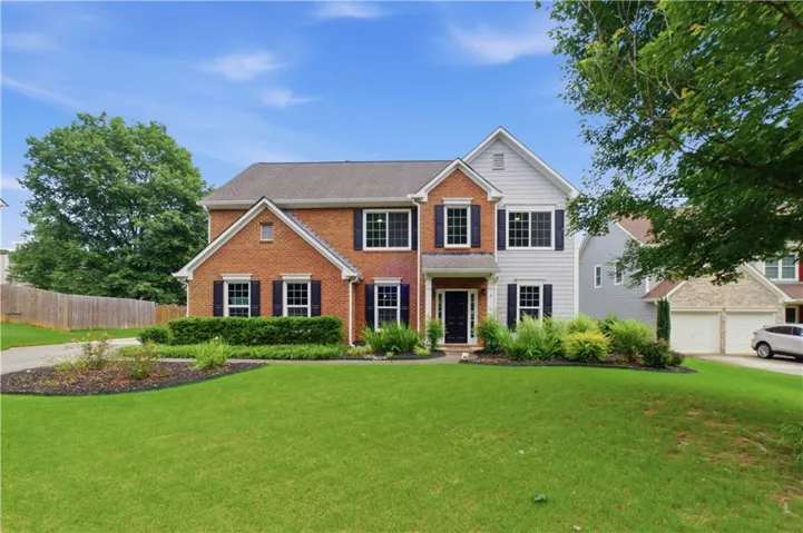 Traditional two-story residence featuring a brick and siding exterior, dark shutters, a front entry door with sidelights, a well-kept front lawn, and established landscaping